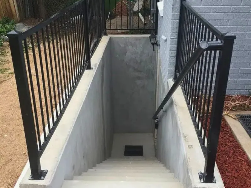 Concrete basement walkout stairwell with metal railings and landing drain