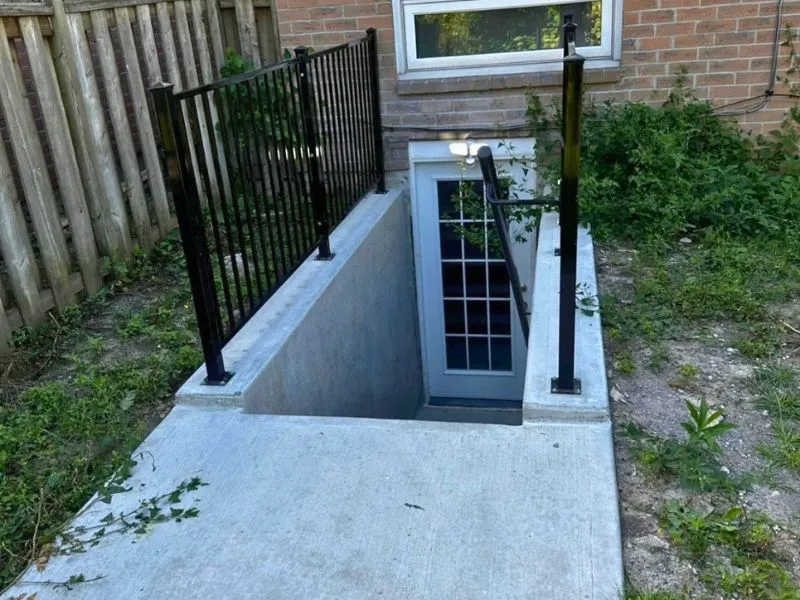 Basement walkout entrance with concrete walls, metal railings and glass door