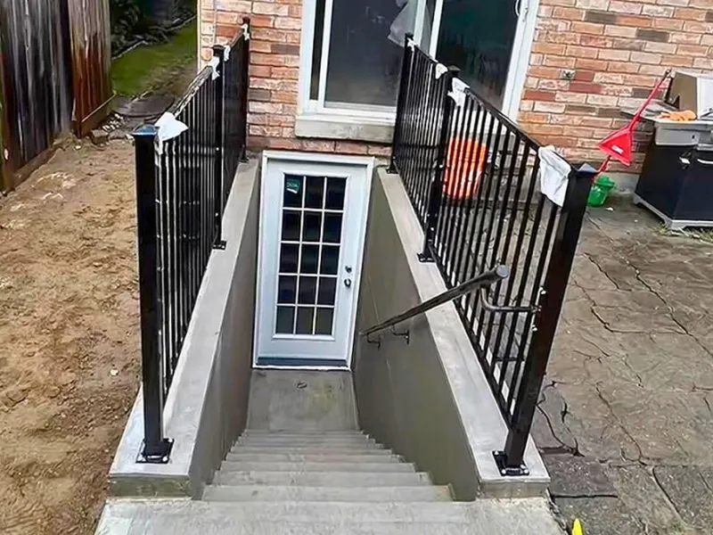 Concrete basement walkout stairs with metal railings and exterior French door